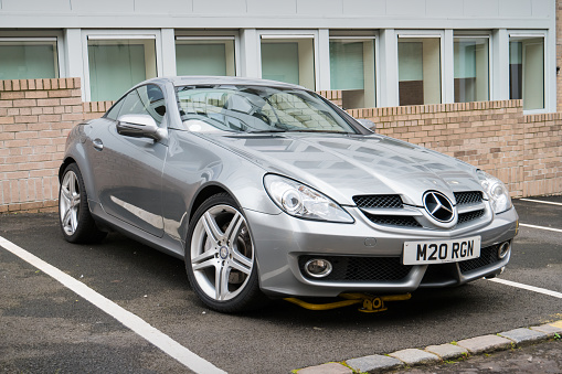 A gray colored second generation Mercedes SLK 200 is parked in a parking lot in Glasgow, Scotland on an overcast day.