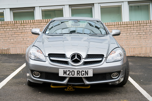 A gray colored second generation Mercedes SLK 200 is parked in a parking lot in Glasgow, Scotland on an overcast day.