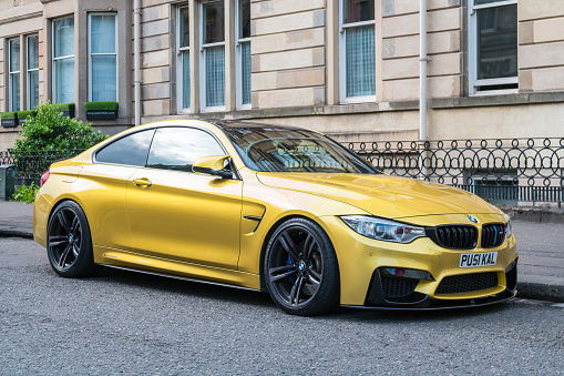 A metallic yellow colored BMW M4 sports car is parked on a street in Glasgow, Scotland, UK on an overcast day.