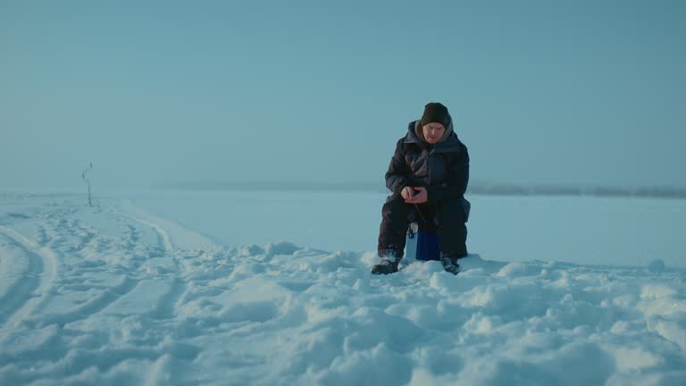 lonely fisherman catching fish in ice hole in middle of frozen river, beautiful landscape, 4K Prores