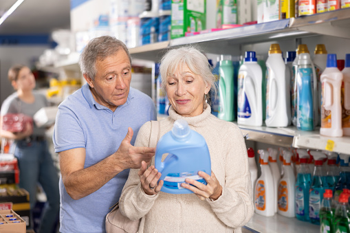 Attentive man and woman purchasers choosing liquid detergent out of large stock in a big supermarket