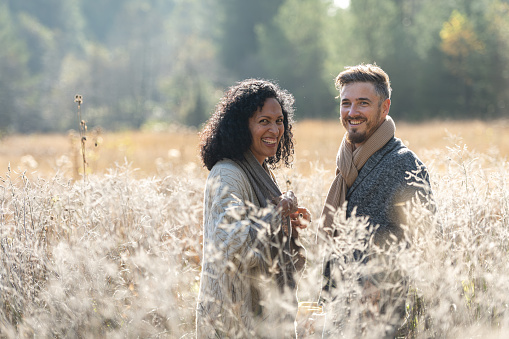 A couple in love, a Latin American woman and a Caucasian man are smilingly running on tall grass with a book in hand and laughing in love. Sunny weather and morning mists, romance.They hold hands and hug. Waist up portrait.