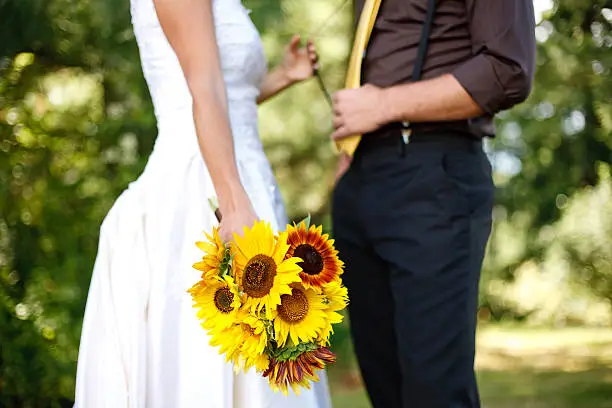 A bride pulling the grooms suspender while holding her bouquet.