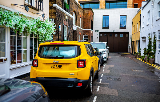 View of a bright yellow car parked on a lovely mews street in the exclusive Belgravia section of London, England.  Flowers decorate the window of the mews home opposite the car.