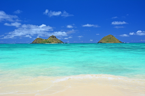 Turquoise waters with a lovely view of the Mokes aka Na Mokulua on a clear sunny day at Lanikai Beach on the windward side of Oahu, Hawaii.