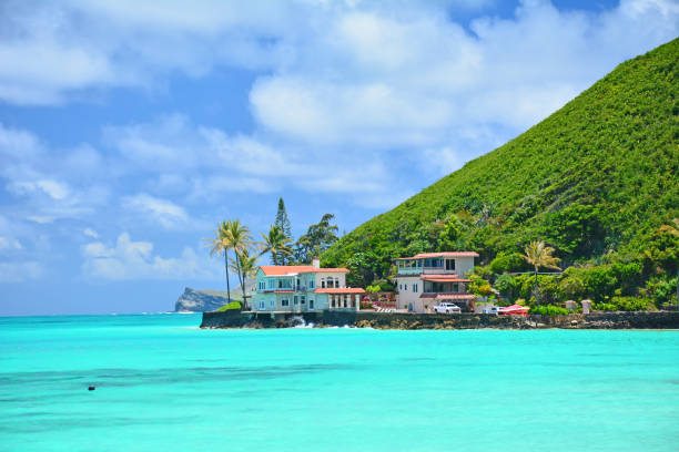 Oceanfront home on a point surrounded by calming turquoise waters on a clear sunny day at Lanikai Beach on the windward side of Oahu, Hawaii.