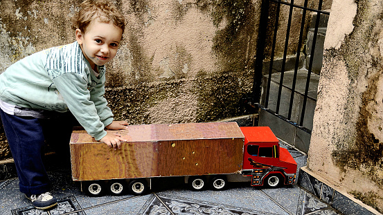 Baby boy playing with his toy truck in the backyard of an old house. The photo was taken outside the residence.