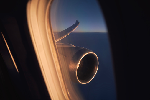 View from window of airplane during flight above clouds at dawn. Selective focus on jet engine and aircraft wing.