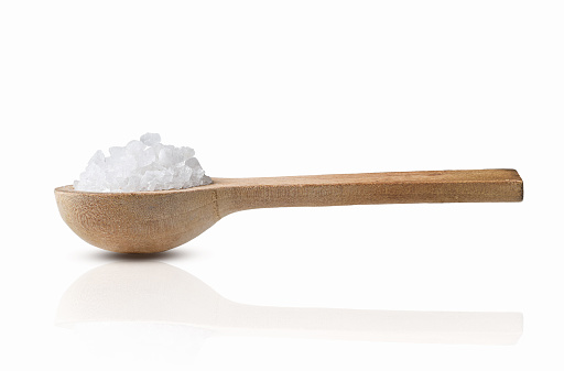 Closeup macro side view of heap of coarse sea salt in a wooden spoon isolated cutout on white background with reflection