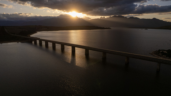 Sunlight casts over a bridge which crosses a large lake. Bridge crossing over the Theewaterskloof dam in the Western Cape, South Africa