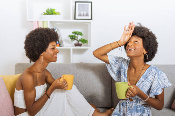 istock Black twin sisters, drinking a cup of coffee, having a happy and expressive conversation, sitting on the living room 1487209396