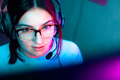 Close-Up Portrait of a Young Woman Wearing Fashionable Eyeglasses and a Headset Microphone Looking at a Computer Monitor with Unique Colorful Vibrant Lighting