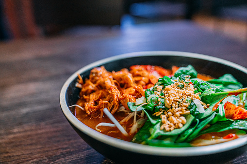 Close-Up Shot of a Bowl of Korean Spicy Kimchee Ramen with Bok Choy and Nuts