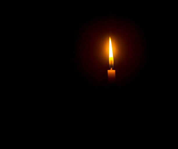 istock A single burning candle flame or light glowing on an orange candle on black or dark background on table in church for Christmas, funeral or memorial service with copy space 1487212801