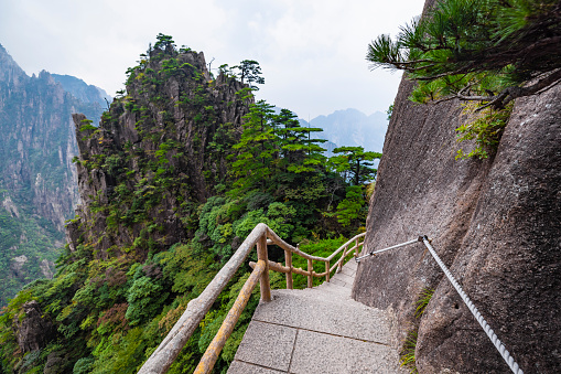 Sanqingshan Mountain in Jiangxi Province, China. A path clinging to the cliff high up on Mount Sanqing with one person walking and enjoying the view.
