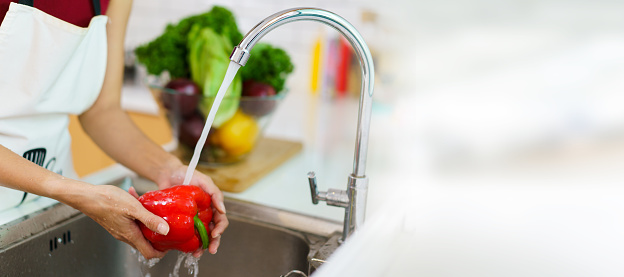 Happy healthy Asian woman washing a vegetables in domestic kitchen faucet before cooking. A housewife preparing and cleaning a fruits and vegetables carefully for cooking a healthy meal.