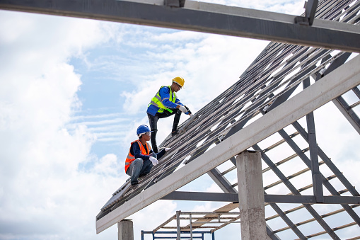 Team of professional construction workers in safety uniforms installing new roofs, with piles of roof tiles for building houses in housing estate industry.