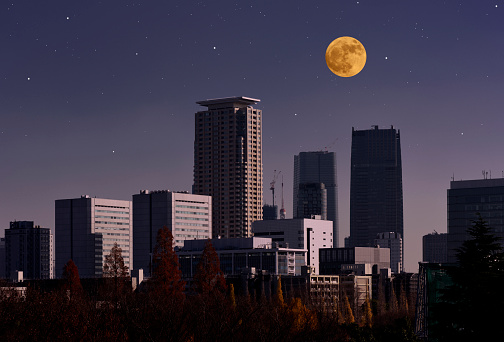 Strawberry full moon rising over the skyscrapers against clear sky with copy space.