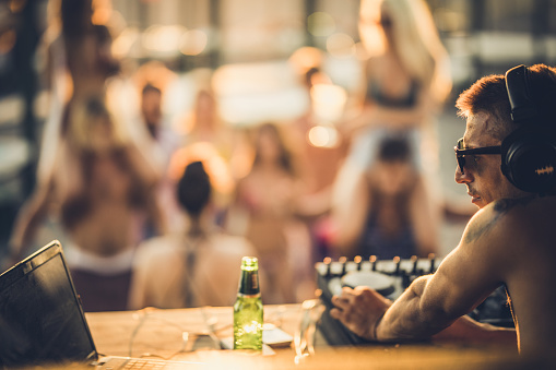 Young DJ playing music on a beach party in summer day.