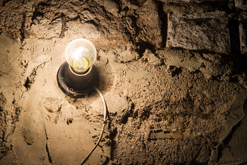 An electric incandescent lamp on an old stone wall. A glowing light bulb on a cracked wall.