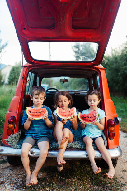 niños sentados en un coche y comiendo rodajas de sandía - camping family vacations eating fotografías e imágenes de stock