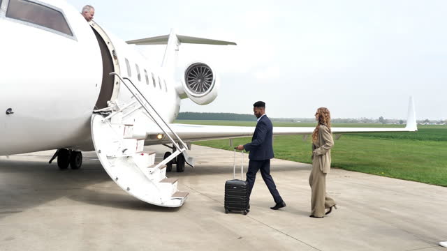 Passengers arriving in private luxury jet near hangar, pilot welcomes the young successful passengers