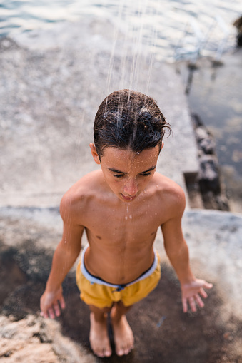 Above shot of Teenage boy taking a outdoors shower after swimming in to the sea