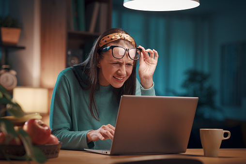 Woman working with her laptop at home, she is lifting her glasses and looking at the computer screen: vision and eye problem concept