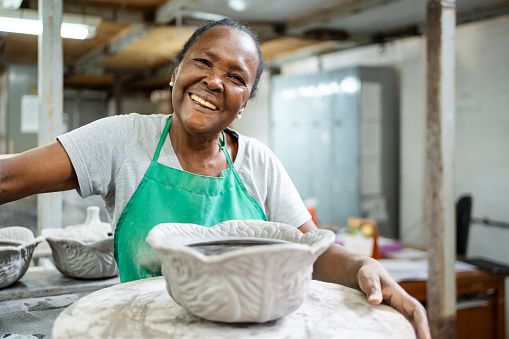 Portrait of a happy senior woman making artistic pottery item in workshop at ceramic factory