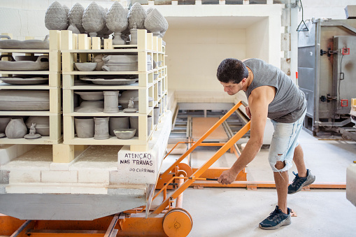 Male worker pushing a rack with many ceramic products into a kiln for firing in a ceramic factory