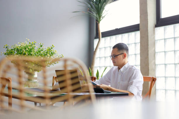 istock An Asian man sits at his dining table, poring over a project document and working on his laptop, illustrating the concept of remote work from home 1487247484
