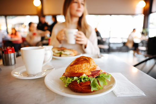 Happy young woman having cafe latte and croissant in cafe