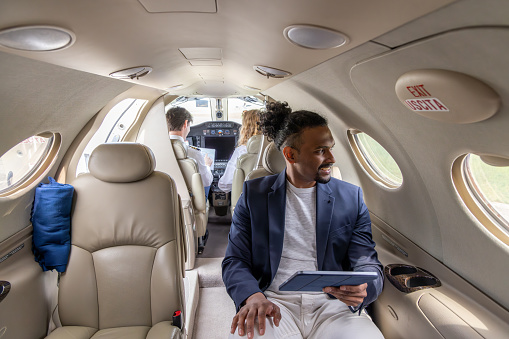 Young businessman working on digital tablet in a private jet plane\nDiversity luxury travel concept