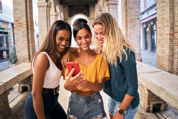 istock Three happy smiling female friends sharing a tablet computer as they stand close together looking at the screen. Multiracial women using mobile smart phone 1487253394