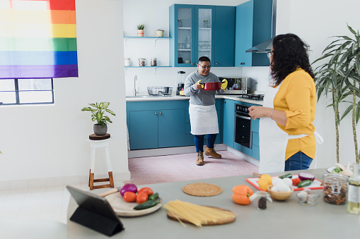 Latin young lesbian couple cooking dinner in kitchen at home in Mexico, Hispanic homosexual people from lgbt community with rainbow flag in Latin America