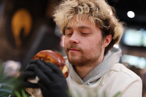 A young guy is ready to eat a juicy burger in fast food.