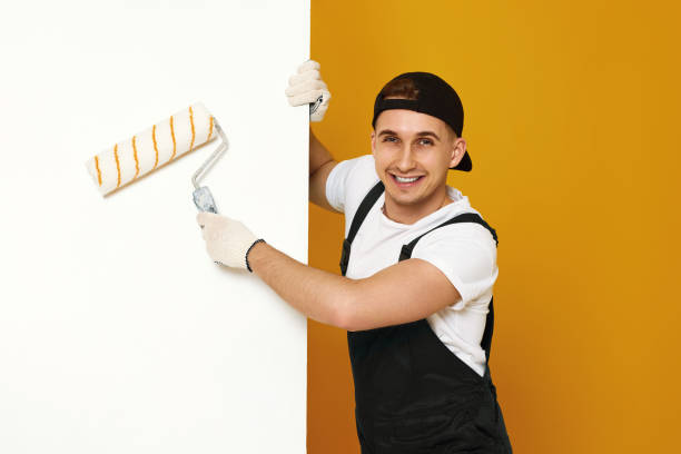 young man in working clothes painting white walls