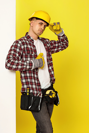 Worker man or builder in construction helmet near white banner on yellow background. building carpentry profession