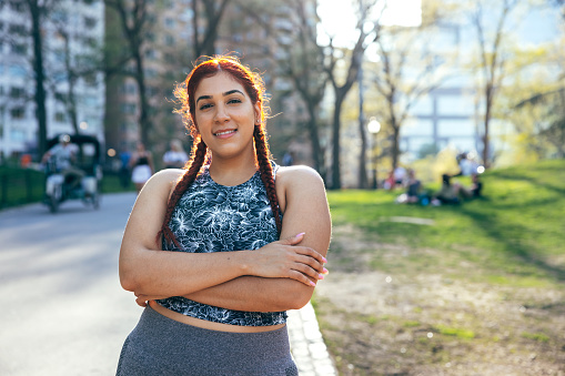 Portrait of a young hispanic woman in sport clothes jogging and enjoying a sunny day in Central Park, New York.