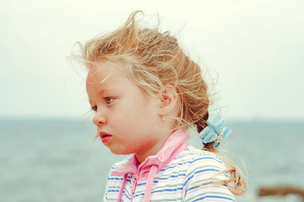 a little girl stands serious in the wind stock photo