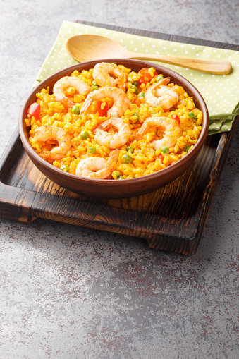 Flavorful Spanish yellow rice and shrimp with vegetables and spices closeup on the plate on the table. Vertical