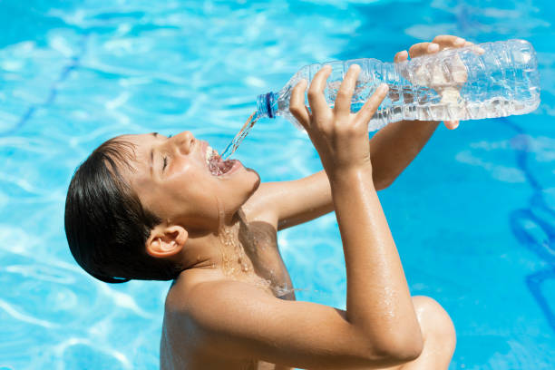 Young man drinking water from a plastic bottle in the pool in summer. person drinking from splashed water bottle to hydrate due to heat wave. Drinking Water for Heat Wave Exhaustion or Heat Stroke
