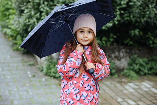 Happy child girl with an umbrella and rubber boots in puddle on an autumn walk