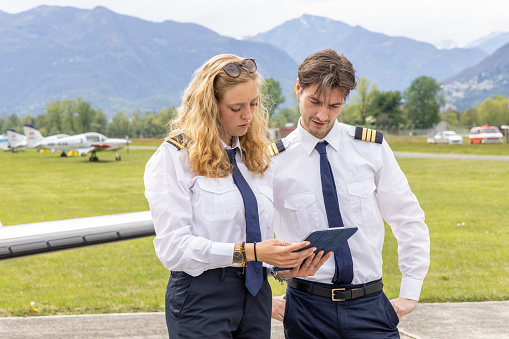 Female and male young pilots preparing private jet for flight\nPilots in the cockpit preparing flight path and check list from digital tablet