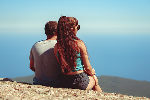 a couple sits on top of a mountain and looks at the sea