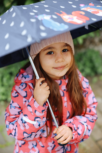 Happy child girl with an umbrella and rubber boots in puddle on an autumn walk