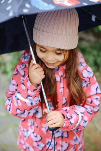 Happy child girl with an umbrella and rubber boots in puddle on an autumn walk