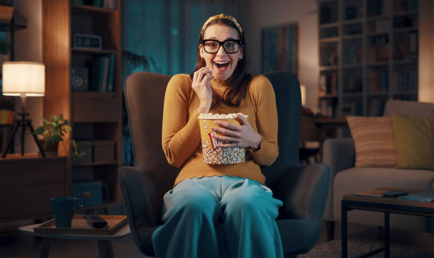 Expressive woman watching TV and eating popcorn stock photo