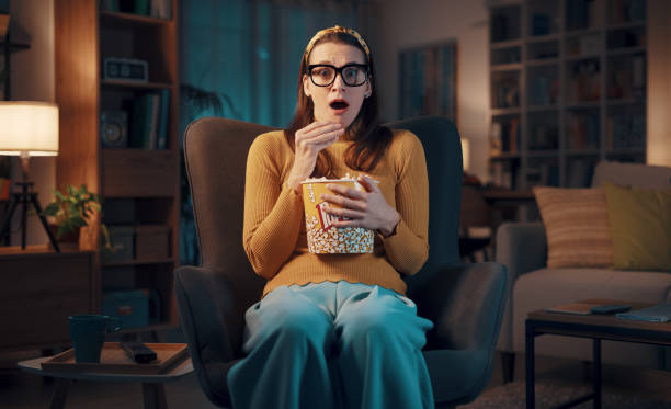 istock Expressive woman watching TV and eating popcorn 1487268010