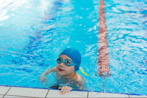 Photo of little caucasian boy wearing goggles looking out from swimming pool